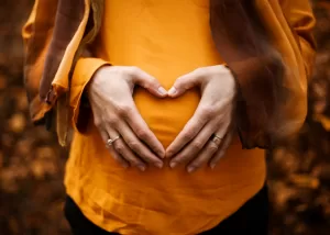 Image shows pregnant woman with hands on belly in heartshape for stress and fertility article